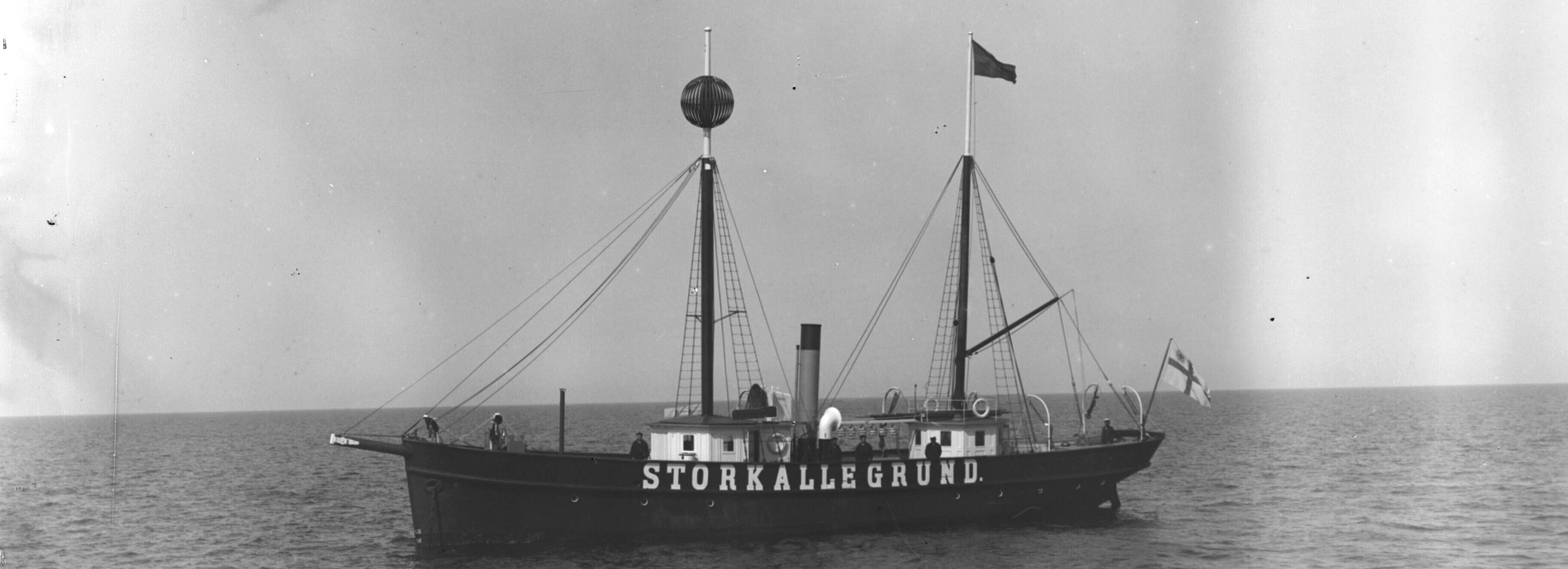 Kuva Majakkalaivasta. Luotsilaitoksen lippu perässä, majakkalippu keskimastossa.