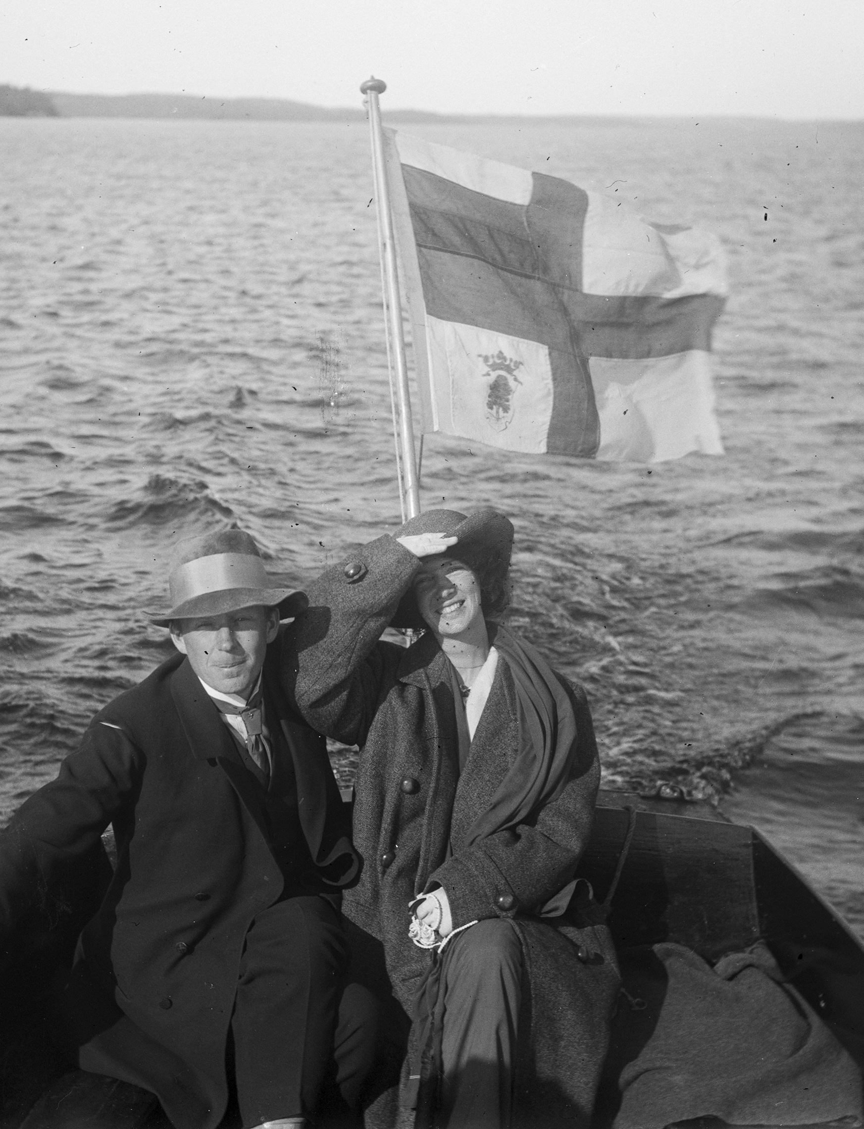 Photo, a man and a woman sitting on a motorboat, yacht flag flying at the rear